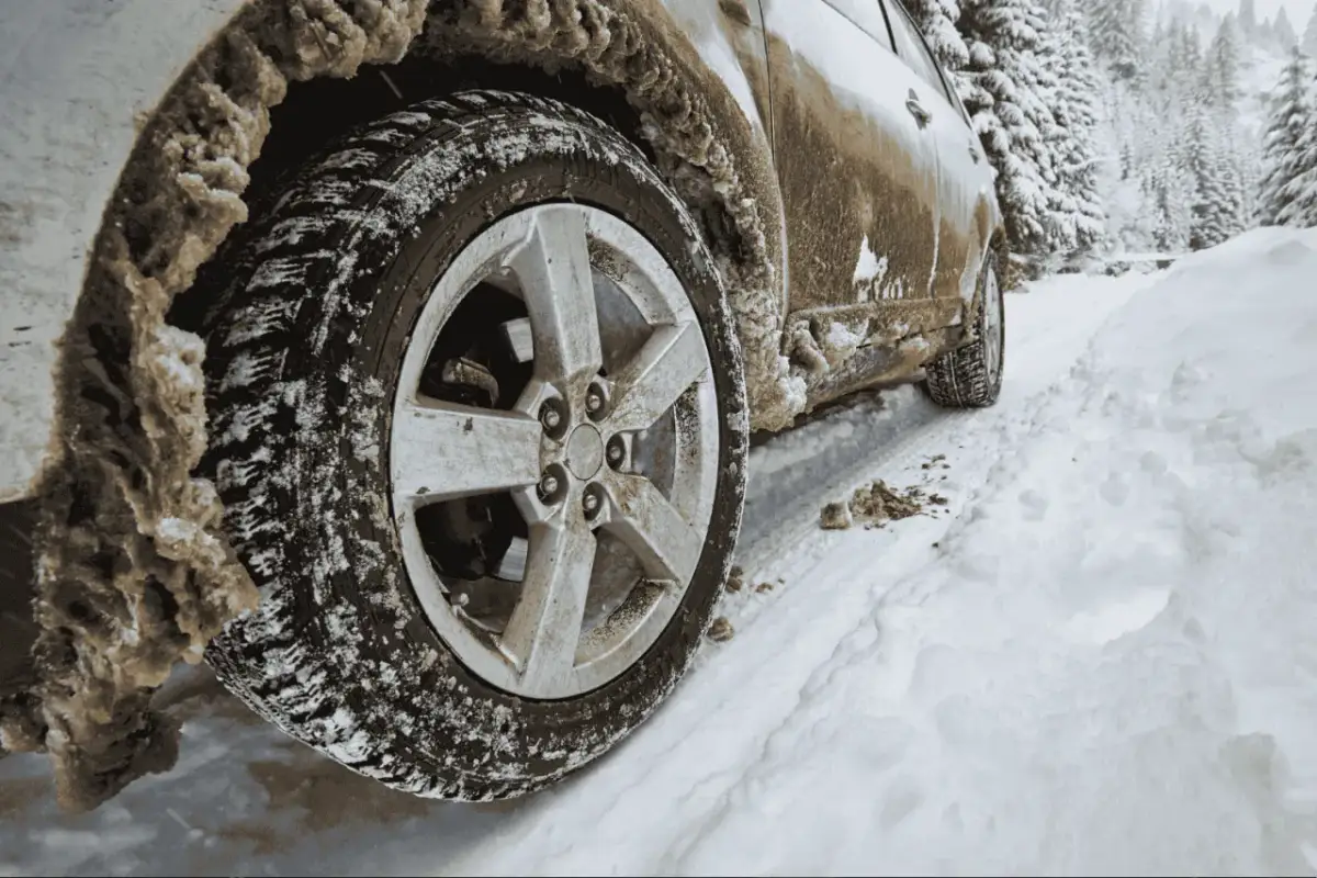 Samochód z napędem 4WD vs AWD na zaśnieżonej drodze. Błoto i śnieg oblepiają koło, sugerując trudne warunki terenowe.