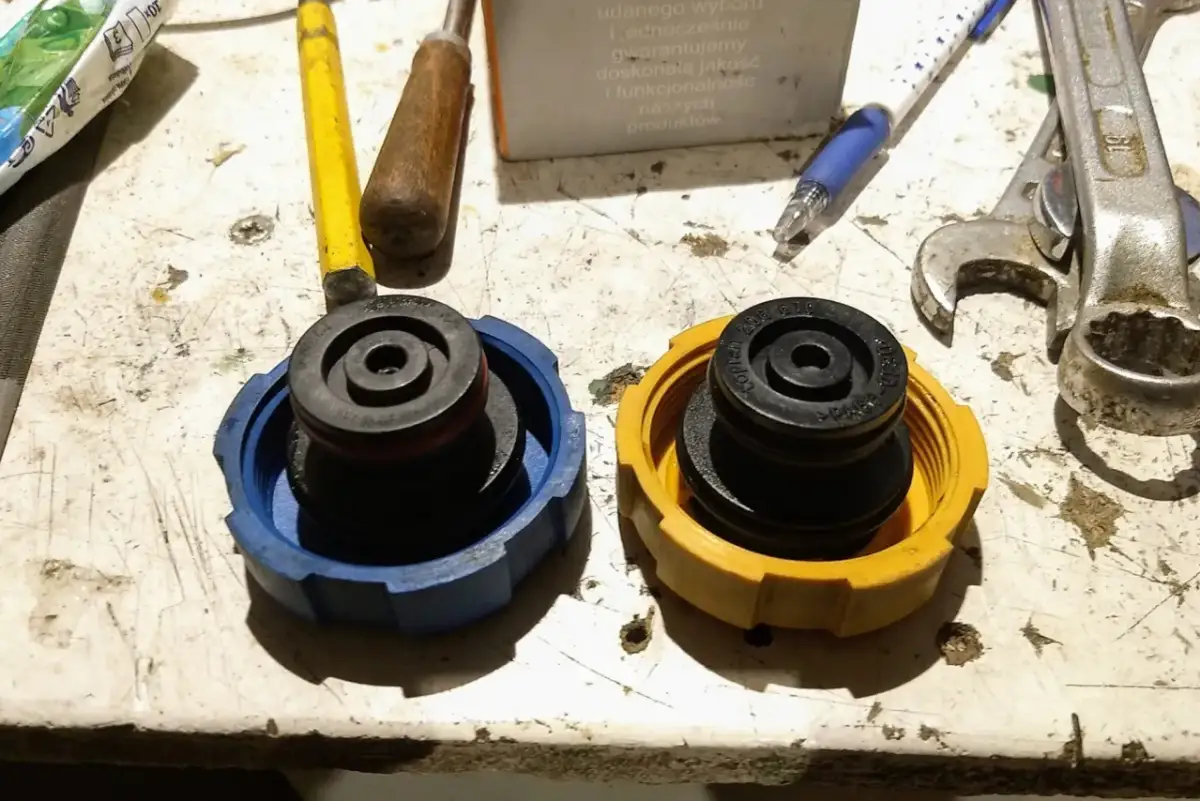 Dwa korki układu chłodzenia, niebieski i żółty, leżą obok narzędzi. Mogą być przyczyną wysokiego ciśnienia w układzie chłodzenia, jeśli są uszkodzone.