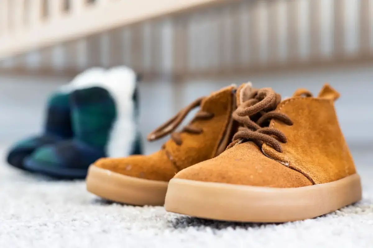 Brązowe, sznurowane buty dziecięce na pierwszym planie, w tle niebiesko-zielone kalosze.