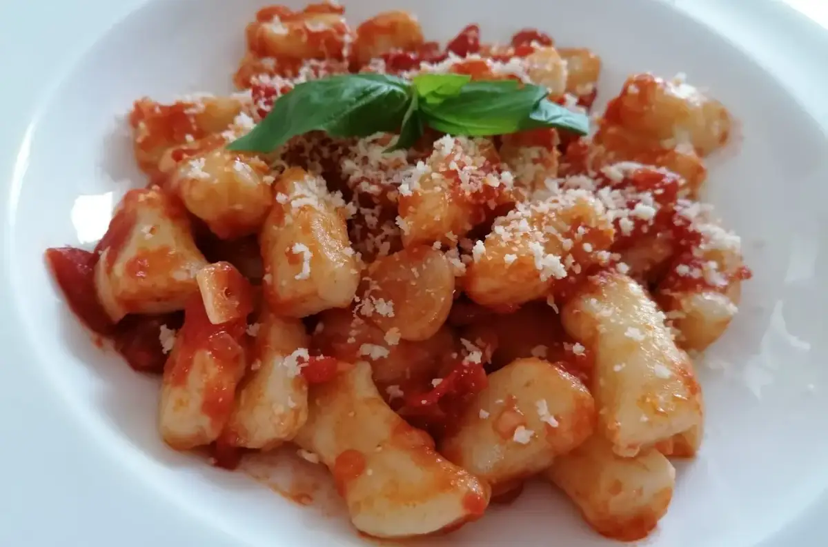 Pyszne gnocchi z sosem pomidorowym, posypane parmezanem i udekorowane listkiem bazylii.