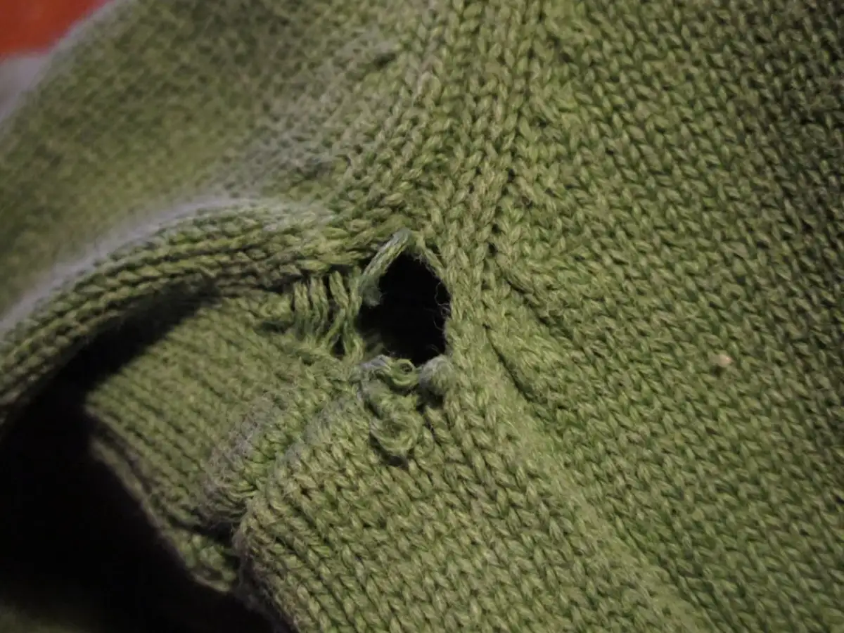 Oczko w zielonym swetrze, które wymaga naprawy. Zobacz, jak łatwo można naprawić oczko w swetrze i przywrócić mu dawny wygląd.
