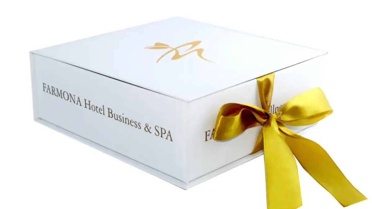 Eleganckie białe pudełko z logo Farmona Hotel Business & SPA, przewiązane złotą wstążką. Idealne na bon do spa.