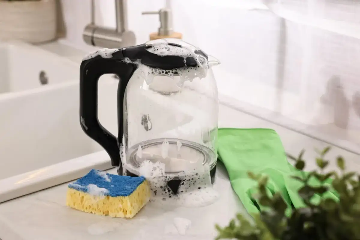 Czajnik w pianie, obok gąbka i rękawica. Prosty sposób, jak odkamienić czajnik octem, by znów lśnił.