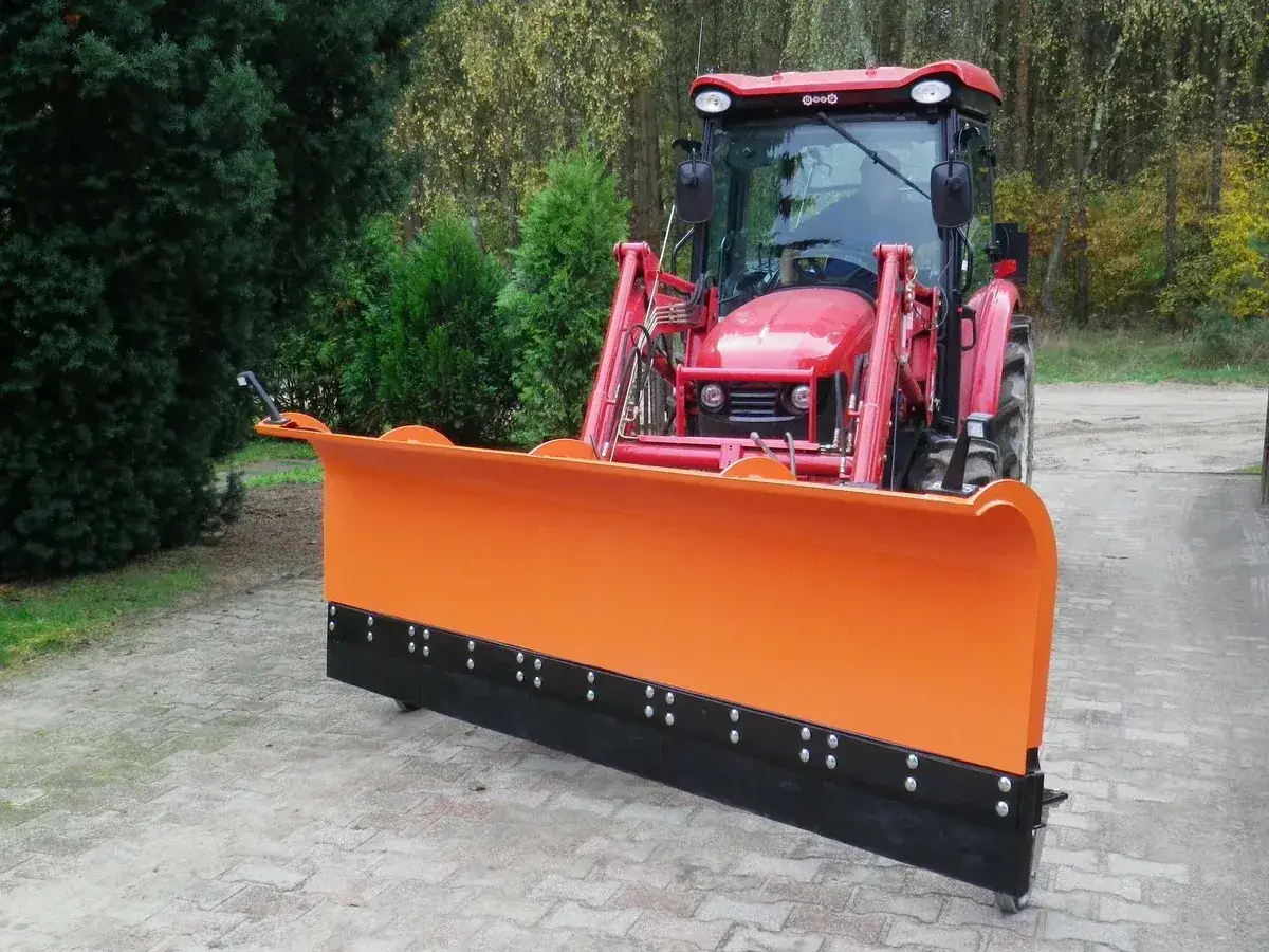 Czerwony traktor z zamontowanym pomarańczowym pługiem do odśnieżania, gotowy do pracy zimą.
