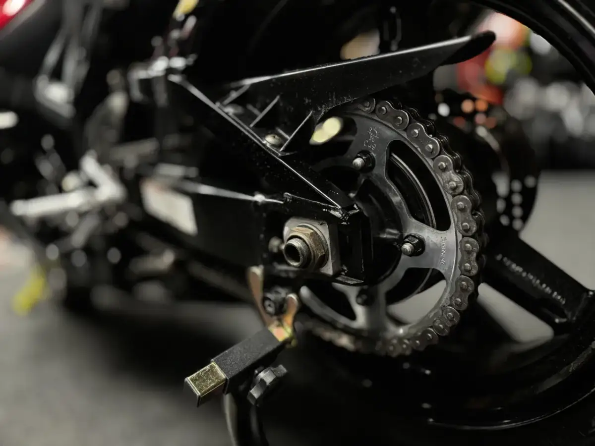 Zbliżenie na tylne koło motocykla z widocznym łańcuchem i zębatką, gotowe do czyszczenia łańcucha motocyklowego.