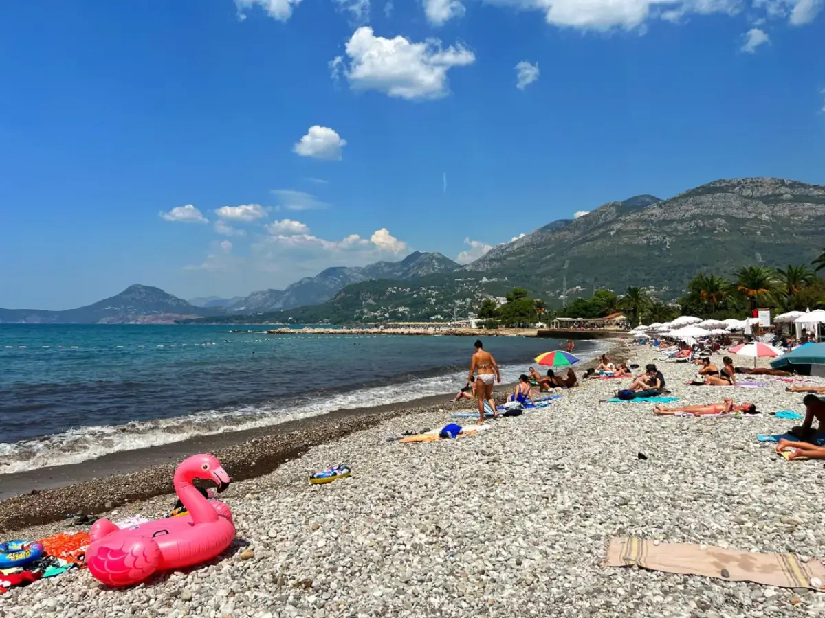 Sutomore atrakcje: plaża z kamienistym brzegiem, turkusowe morze i góry w tle. Różowy flaming na piasku zaprasza do relaksu.