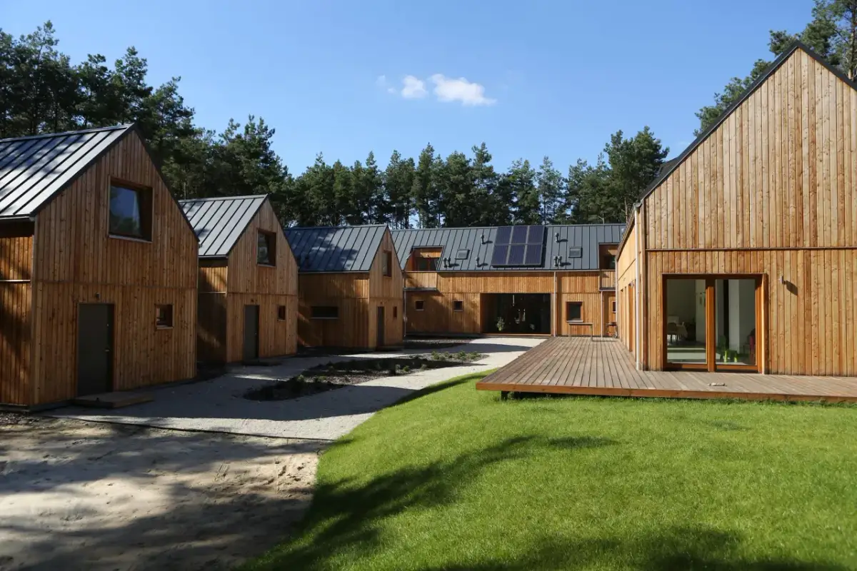 Drewniane domy z panelami słonecznymi otoczone lasem, z trawnikiem i tarasem.