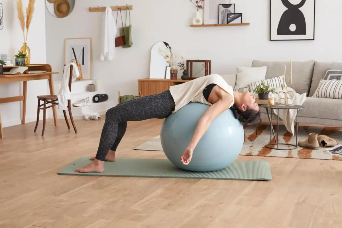 Kobieta wykonuje ćwiczenia na piłce gimnastycznej, rozciągając mięsień prosty brzucha.