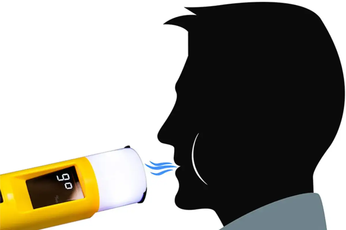 Alkomat pokazuje 0,90 mg/l. Mężczyzna dmucha w urządzenie, sprawdzając poziom alkoholu.