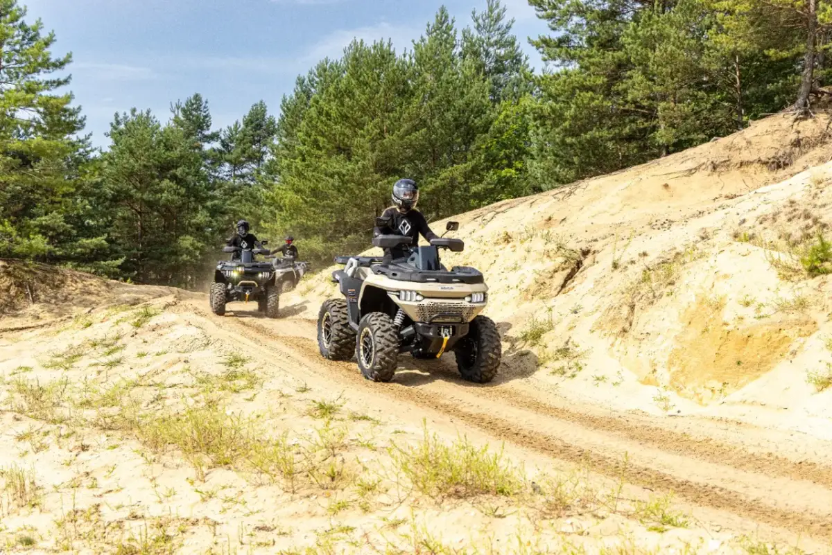 Trzy quady jadące po piaszczystej drodze w lesie. Pamiętaj o regularnej wymianie oleju w quadzie, by zapewnić mu długą żywotność.