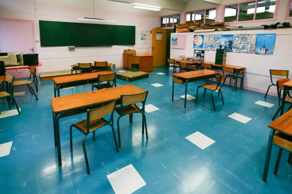 Pusta klasa szkolna z rzędami drewnianych ławek i krzeseł na niebieskiej podłodze.