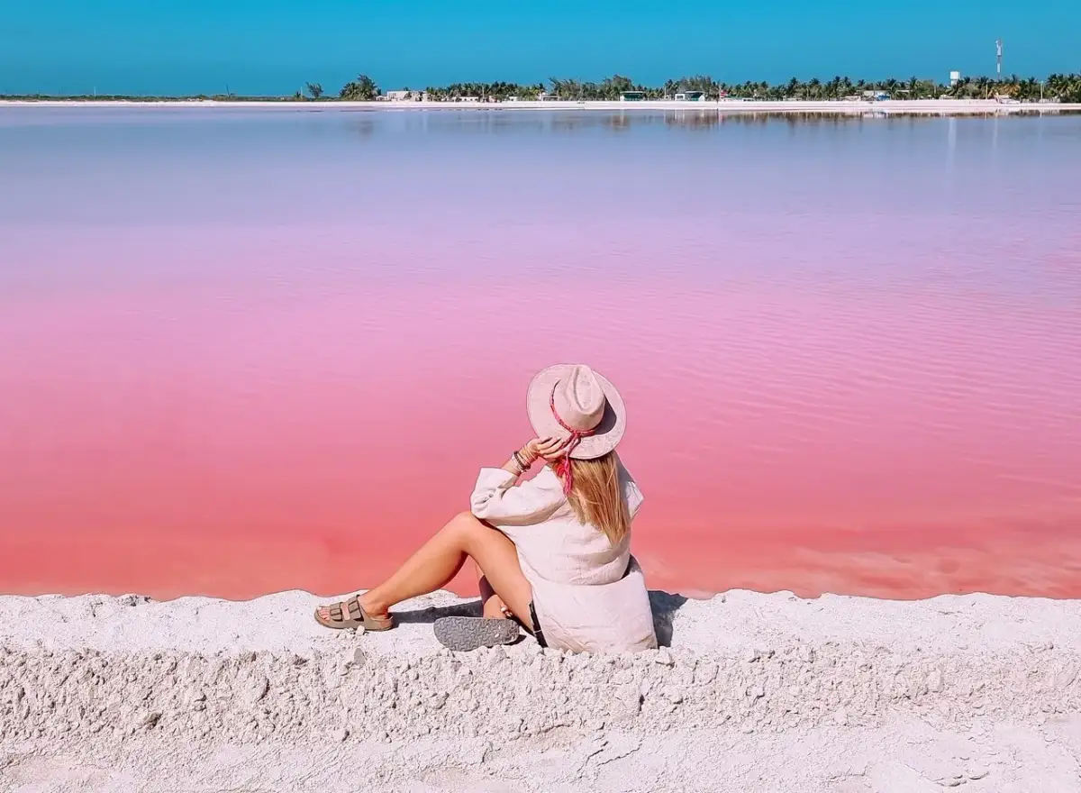 Kobieta w kapeluszu siedzi na piasku, podziwiając niezwykłą, różową plażę w Meksyku.