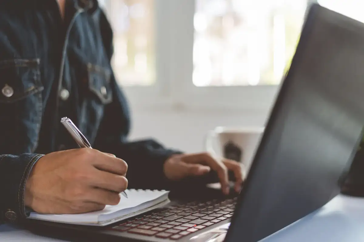 Osoba w dżinsowej kurtce pisze w notatniku, analizując wskaźnik rentowności kapitału własnego.