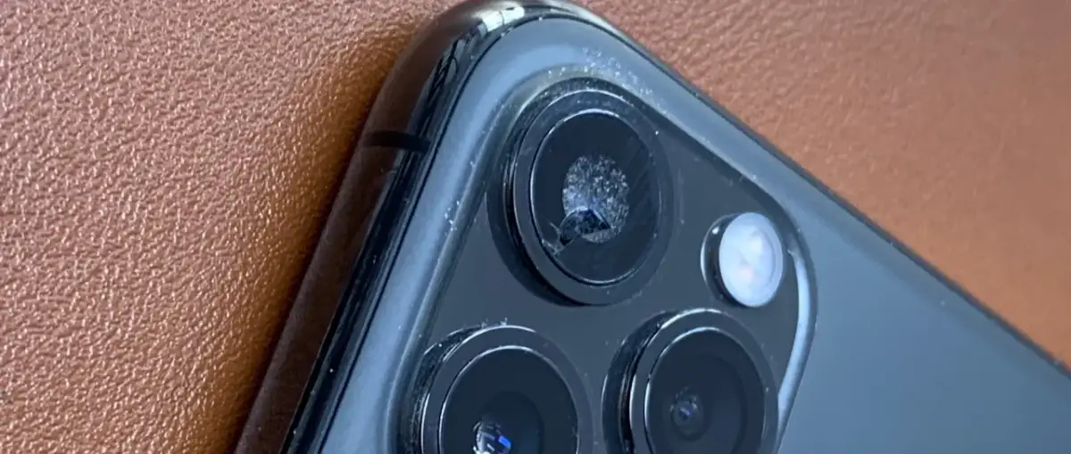 Zbliżenie na pęknięte szkło aparatu iPhone'a na brązowym tle.