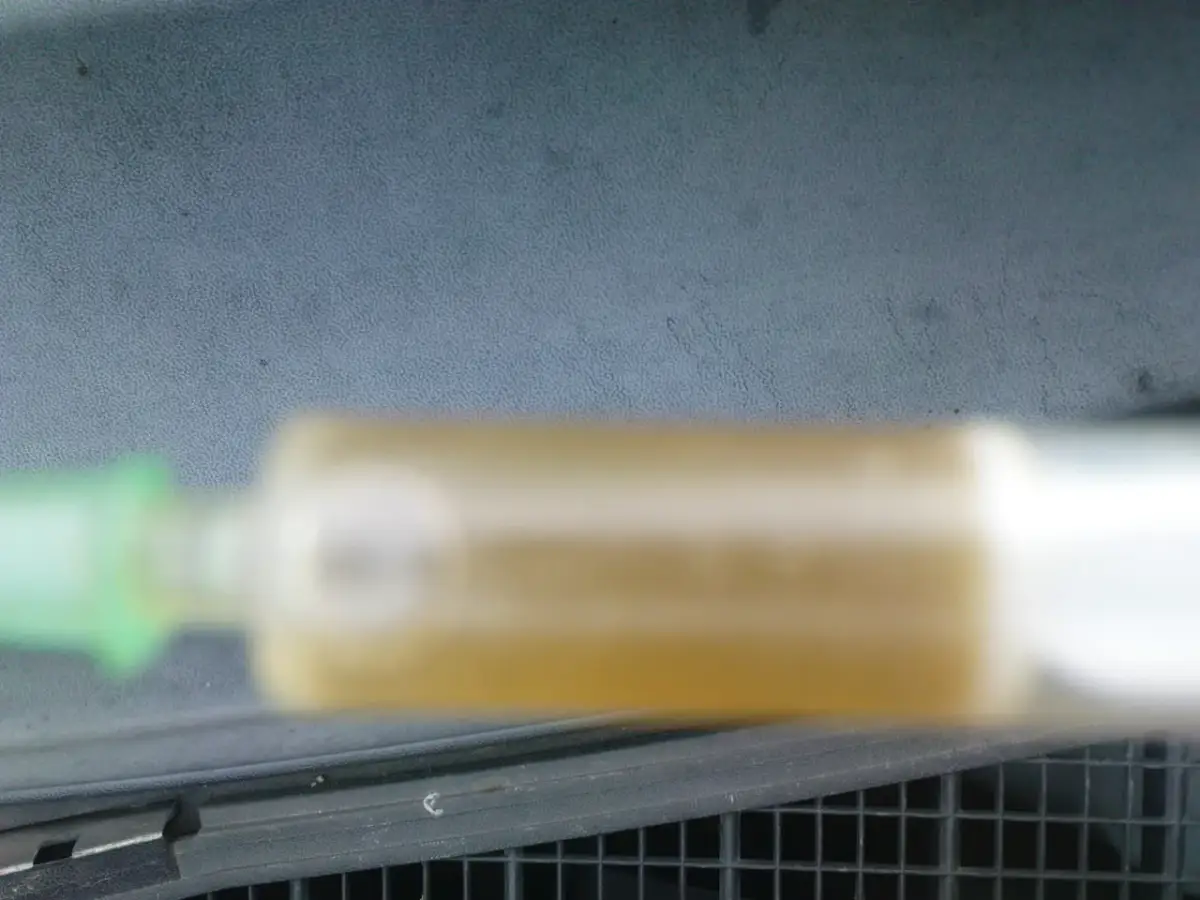 Strzykawka z żółtym płynem chłodniczym na tle deski rozdzielczej.