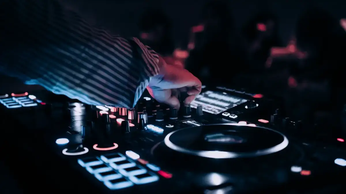 Dłoń DJ-a regulująca pokrętła na konsoli, w tle rozmyte światła.