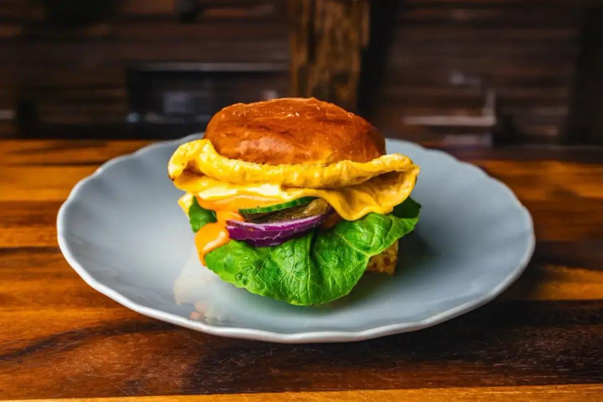 Soczysty burger z serem, sałatą, ogórkiem i czerwoną cebulą na talerzu.