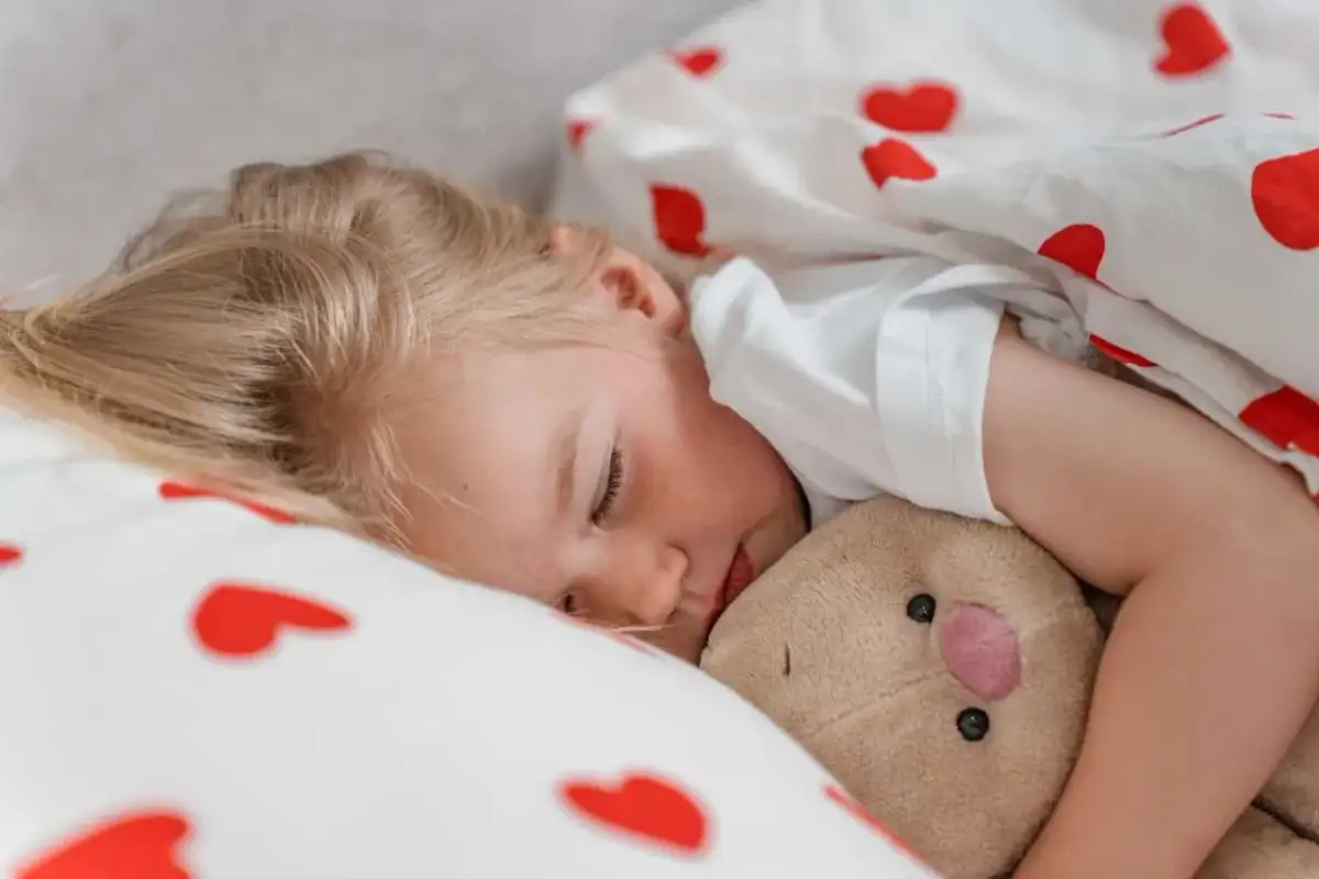 Śpiące dziecko przytula misia. Marzy o dniu pełnym słońca i zabawy, może nawet o nauce pływania w swojej pianka do pływania dla dziecka.