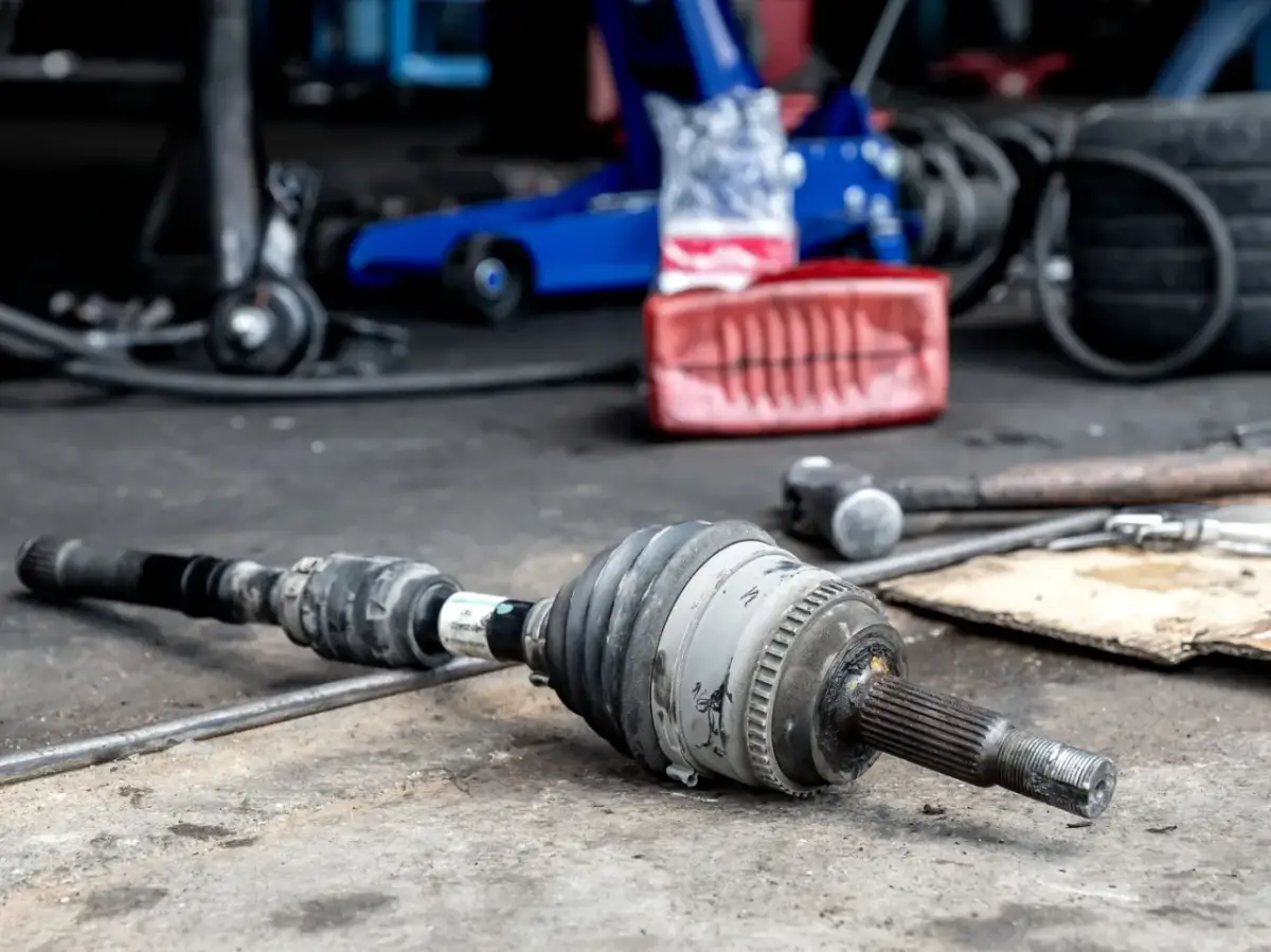 Uszkodzona półoś objawy: stukanie przy skręcaniu, wibracje. Część leży na podłodze warsztatu obok narzędzi.