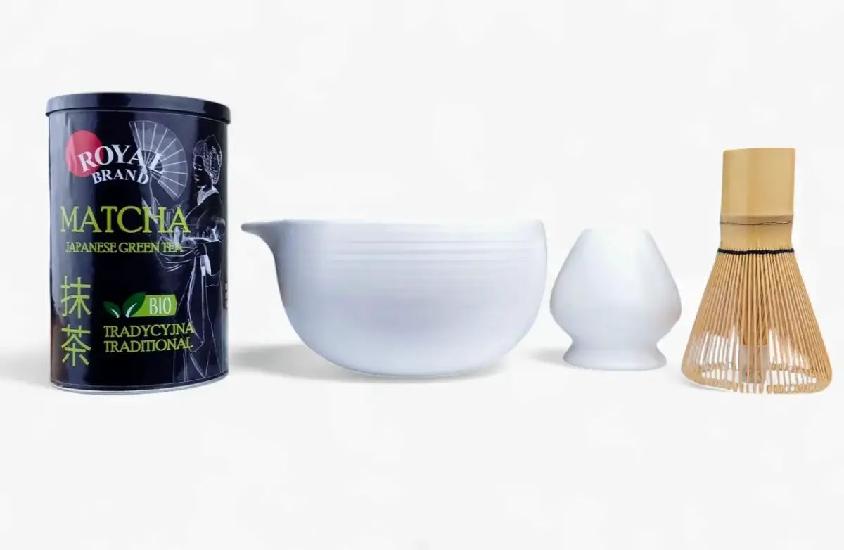 Zestaw do przygotowania herbaty matcha: puszka z zieloną herbatą, biała miseczka i bambusowa miotełka.