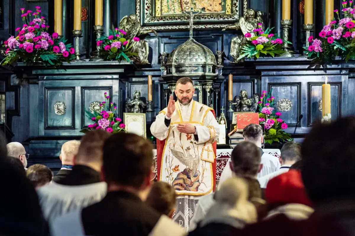 Kapłan w kościele, przed ołtarzem z kwiatami, błogosławi wiernych. W tle widać ozdobne zdobienia i świece. Jasna Góra intencje mszalne.
