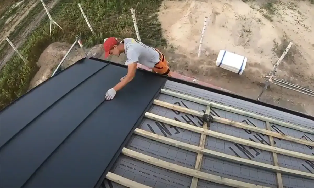 Pracownik montuje czarną blachę na dachu altanki. Nowy dach zapewni ochronę przed deszczem.