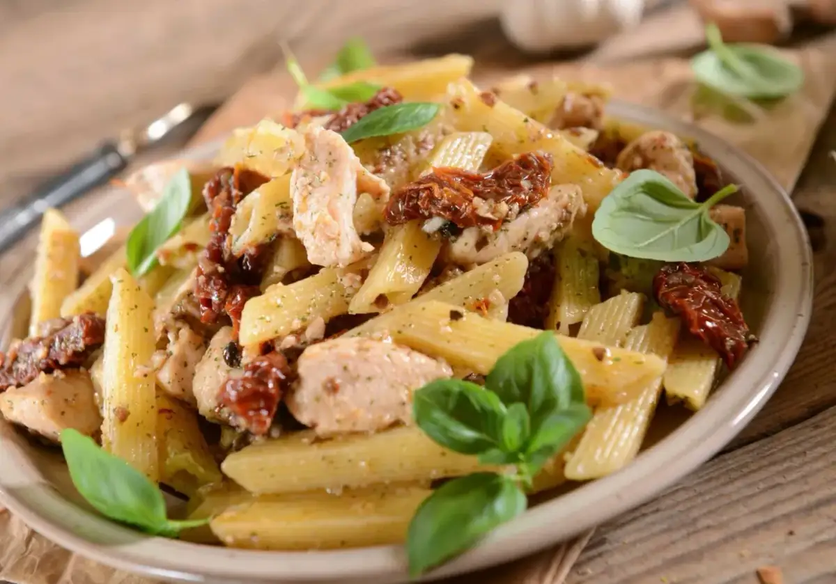 Penne z kurczakiem i suszonymi pomidorami, udekorowane świeżą bazylią. Pyszne danie, które zachwyci każdego smakosza.