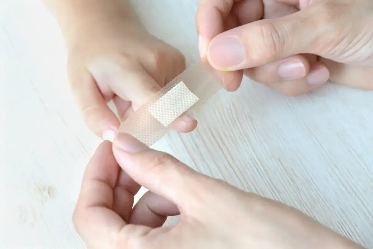 Ręce przyklejają plaster na palec dziecka, by pomóc mu jak oduczyć dziecko ssania palca przy zasypianiu.