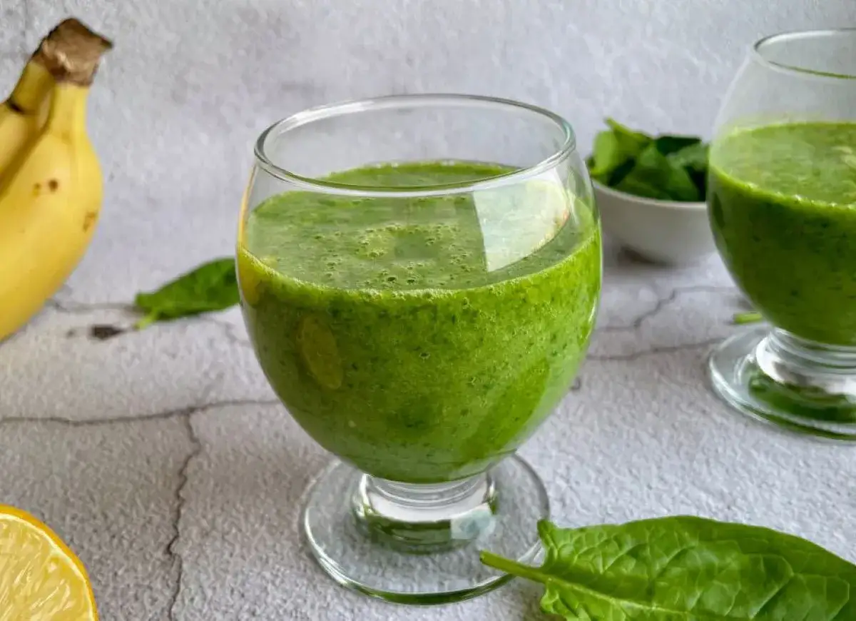 Zielony koktajl ze szpinakiem, bananem i cytryną w szklance. Obok leżą świeże liście szpinaku i połówka cytryny.