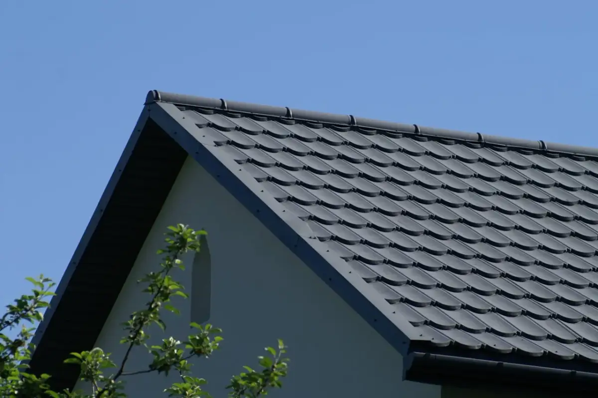 Szary dach z dachówki ceramicznej, idealny do obliczenia, ile dachówek na m2 roben. W tle błękitne niebo i fragment ściany domu.