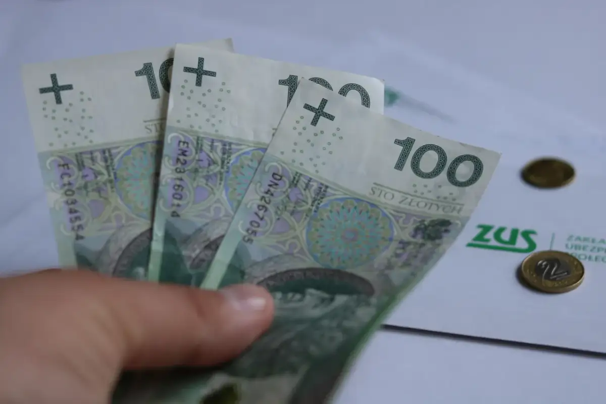 Dłoń trzyma banknoty 100 zł. Na papierze ZUS i monety. Czy to wystarczy na rentę na kręgosłup?