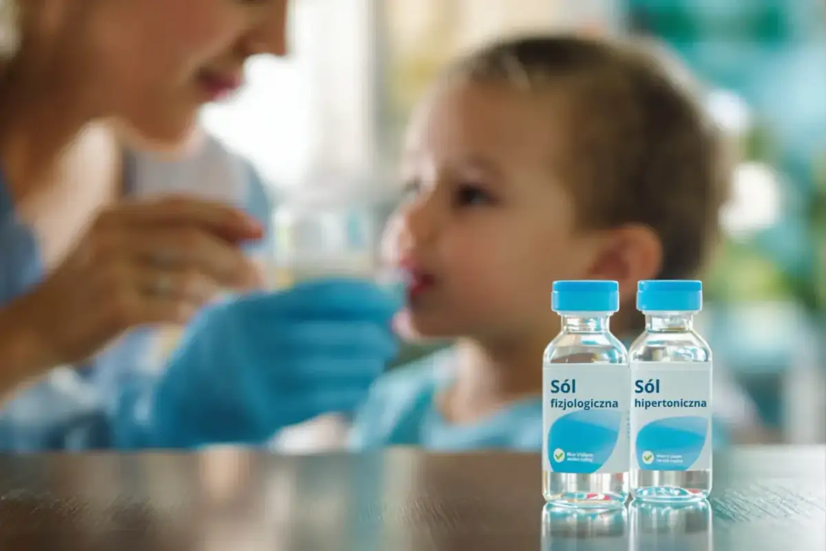 Dwie buteleczki soli fizjologicznej do nosa, w tle kobieta podająca płyn dziecku.