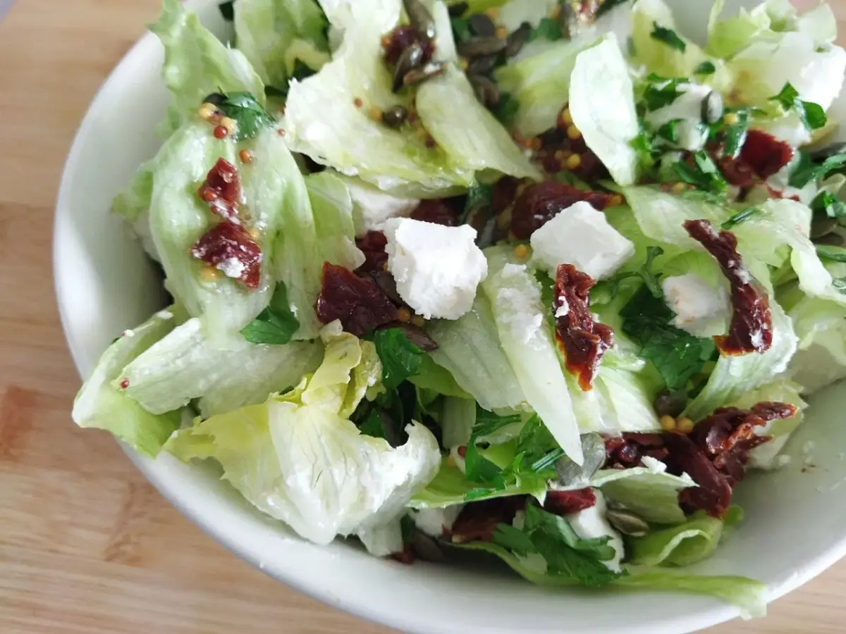 Pyszna surówka z sałaty lodowej z fetą, suszonymi pomidorami i pestkami dyni. Idealna na szybki obiad.