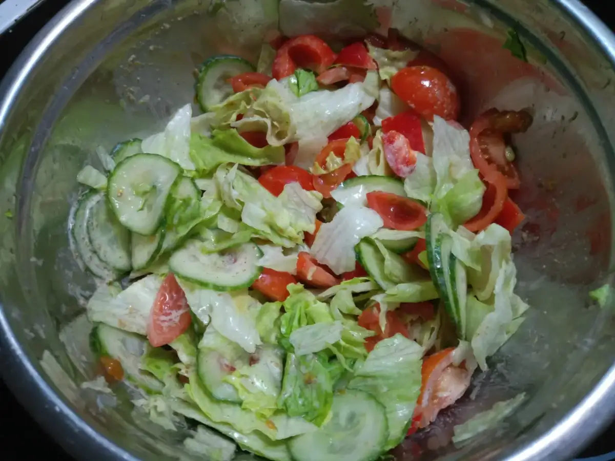 Sałatka z sałaty, pomidorów i ogórka w metalowej misce, polana sosem.