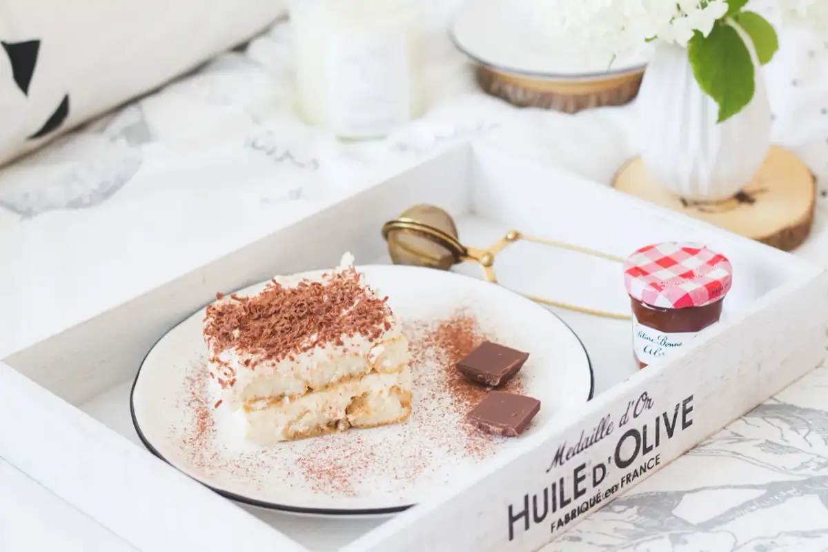 Pyszne tiramisu z biszkoptami, posypane kakao i czekoladą, na tacy z dżemem i kwiatami. Idealne na leniwe popołudnie.