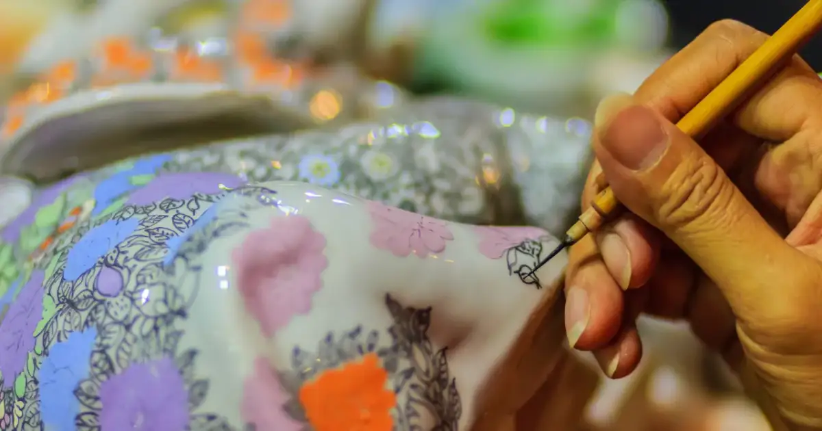 Dłoń maluje cienkim pędzelkiem wzory na ozdobionej porcelanie.