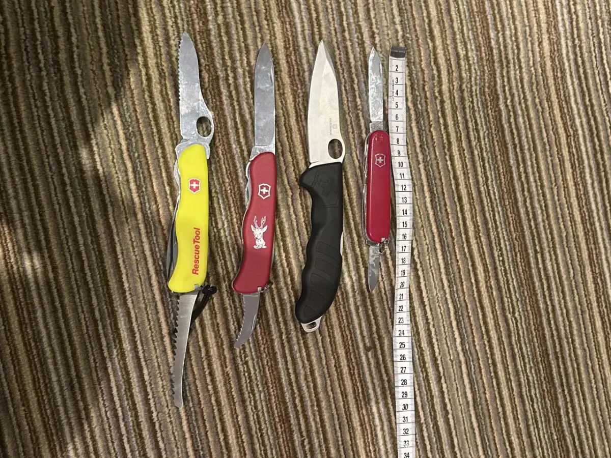 Cztery scyzoryki, w tym jeden z napisem "Rescue Tool", leżą obok miarki. Czy można przewozić nóż w bagażu rejestrowanym?