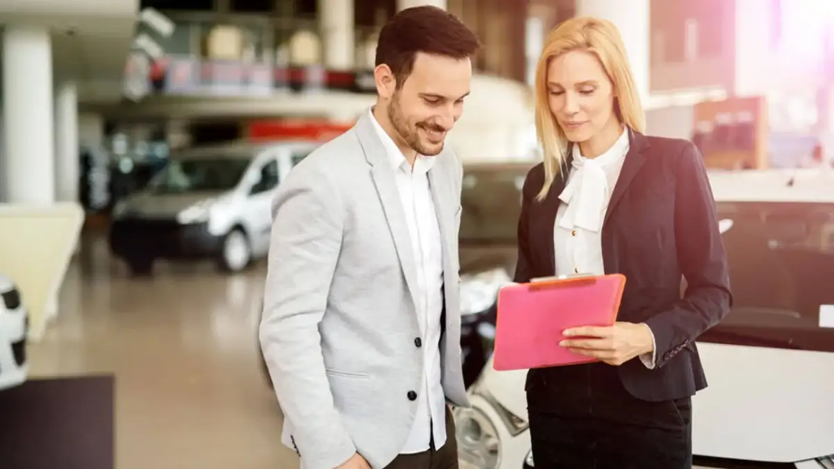 Mężczyzna i kobieta w salonie samochodowym omawiają wykup z leasingu na cele prywatne. Kobieta trzyma różową teczkę.