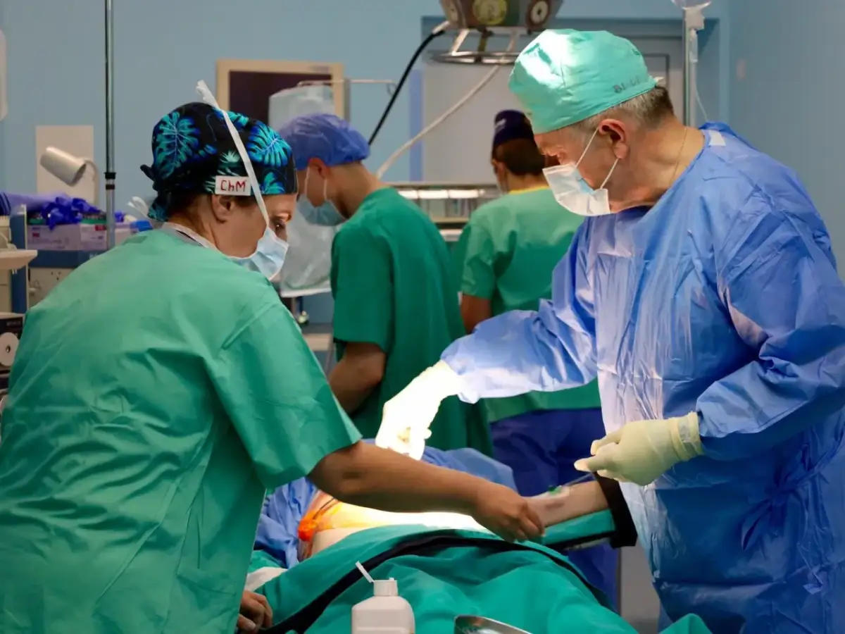 Chirurdzy w maseczkach i czepkach operują pacjenta na stole.