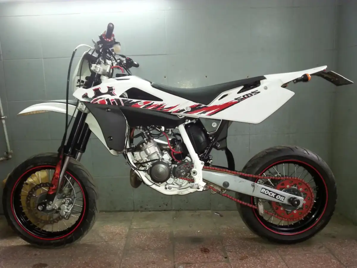 Biały motocykl Husqvarna 125 supermoto z czerwonymi akcentami i napędem. Gotowy do jazdy po mieście i torze.