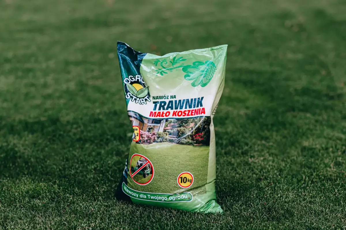 Zielona torba z nawozem do trawnika na tle trawy.