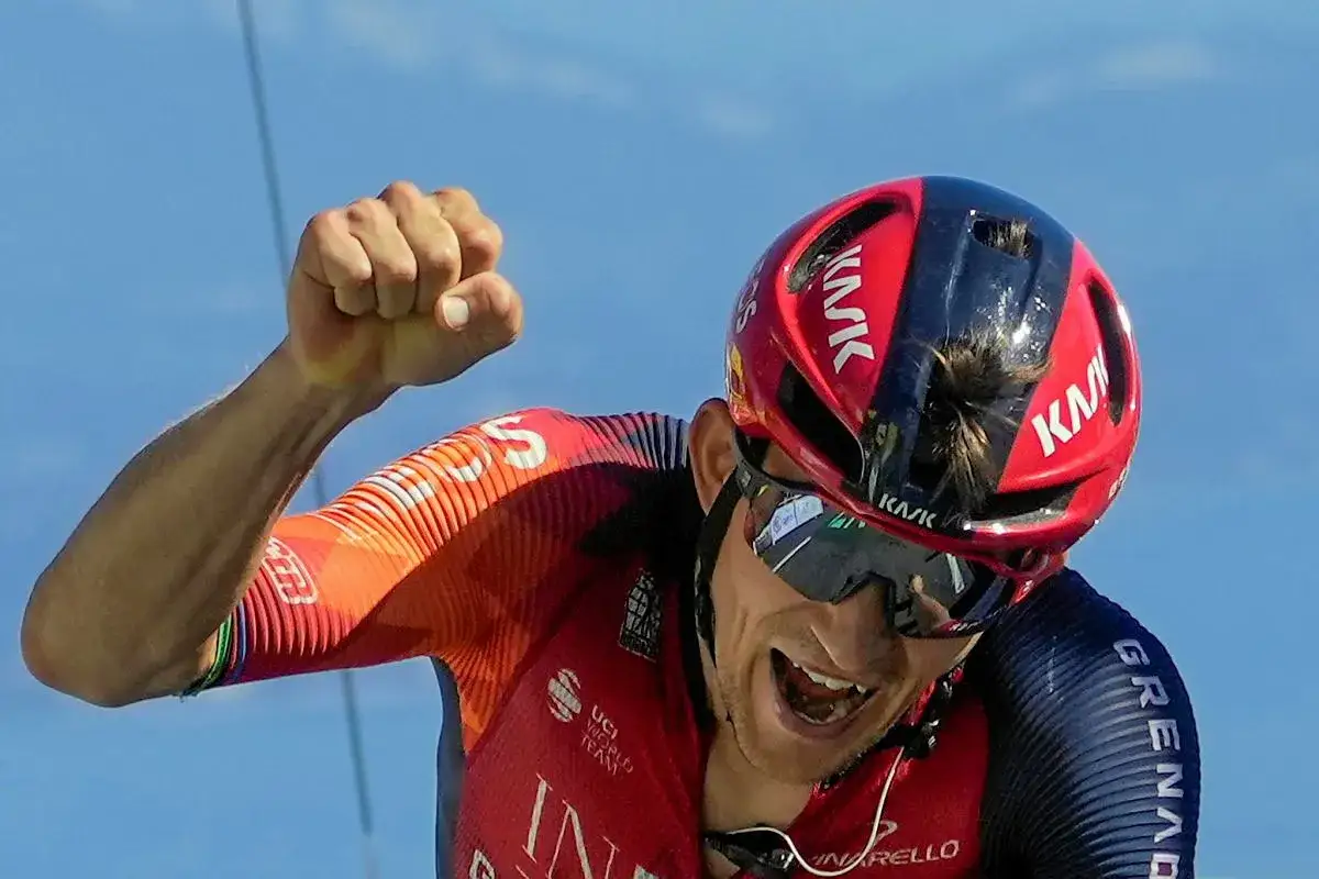 Michał Kwiatkowski, kolarz, triumfuje z zaciśniętą pięścią na tle błękitnego nieba.