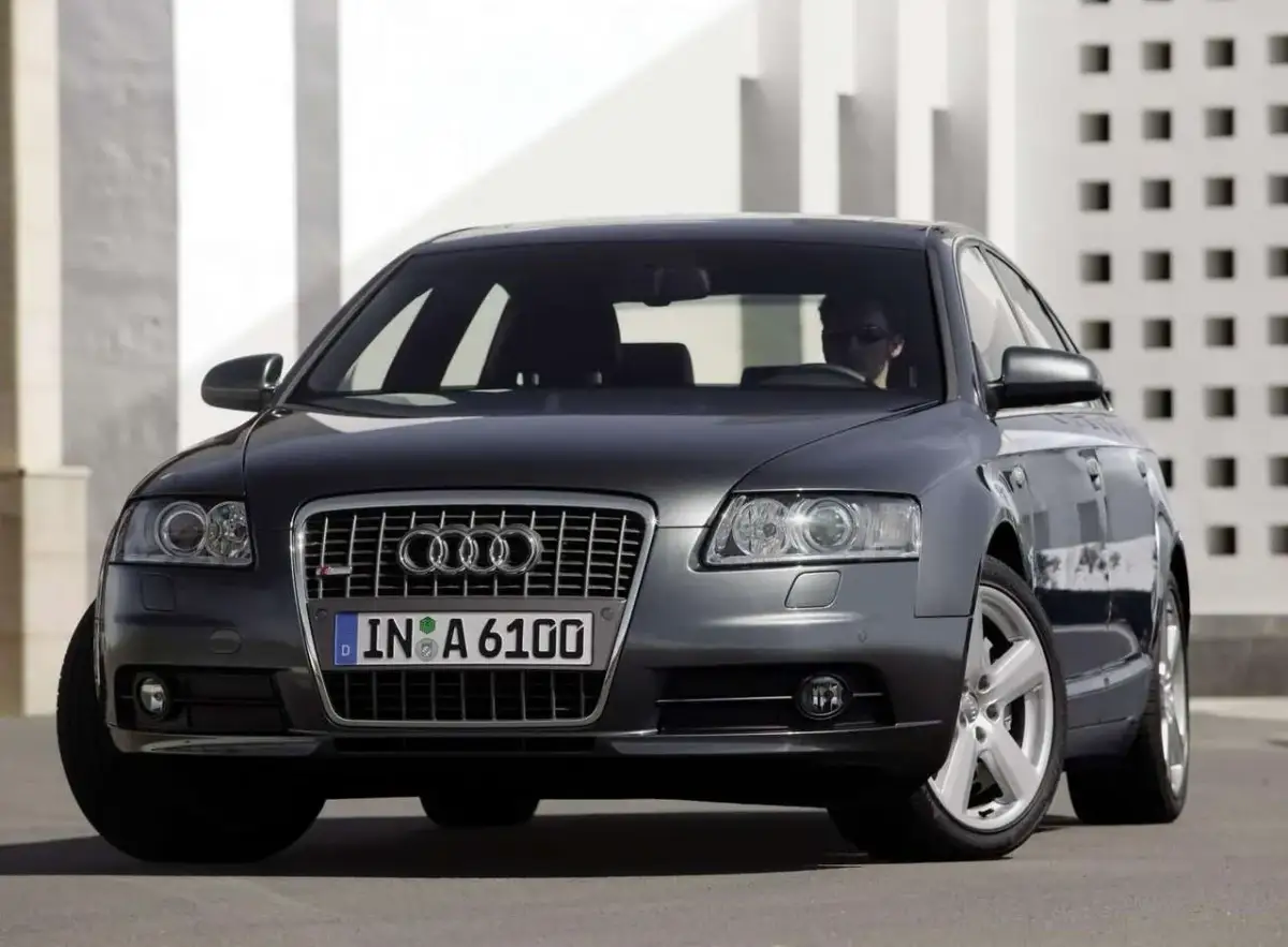 Elegancki, ciemnoszary Audi A6 C6 z przyciemnianymi szybami i chromowanymi felgami, zaparkowany przed nowoczesnym budynkiem.