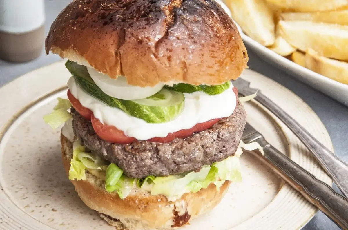 Domowy hamburger z soczystym kotletem, warzywami i frytkami w tle.