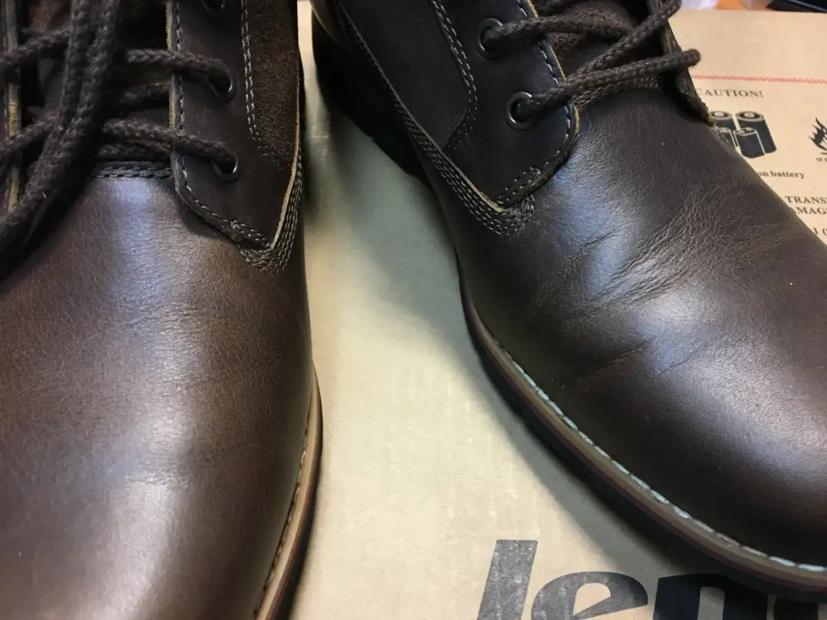 Brązowe, skórzane buty z ciemnymi sznurówkami. Skóra na jednym bucie jest lekko pognieciona, co może sugerować potrzebę dowiedzenia się, jak wyprostować skórę na butach.