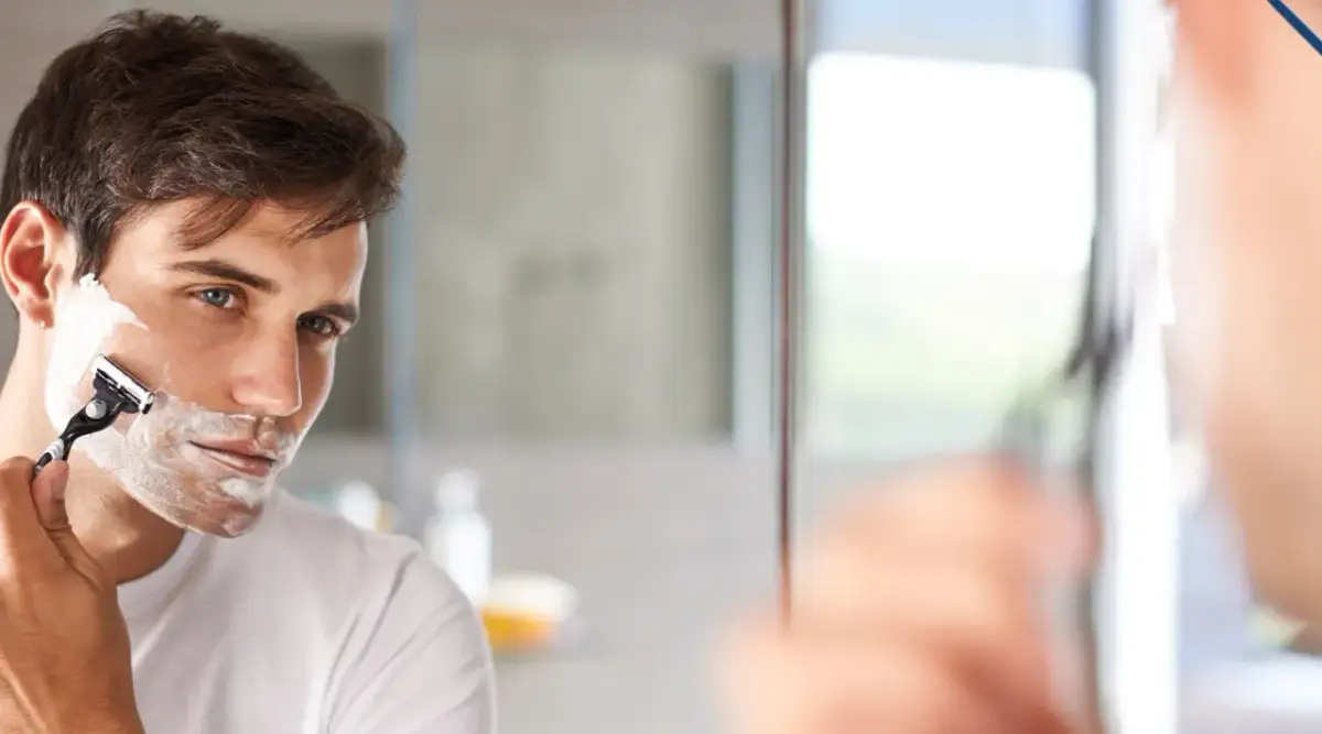Mężczyzna goli twarz pianką. Czy woda toaletowa to to samo co woda po goleniu? Zastanawia się nad tym, patrząc w lustro.