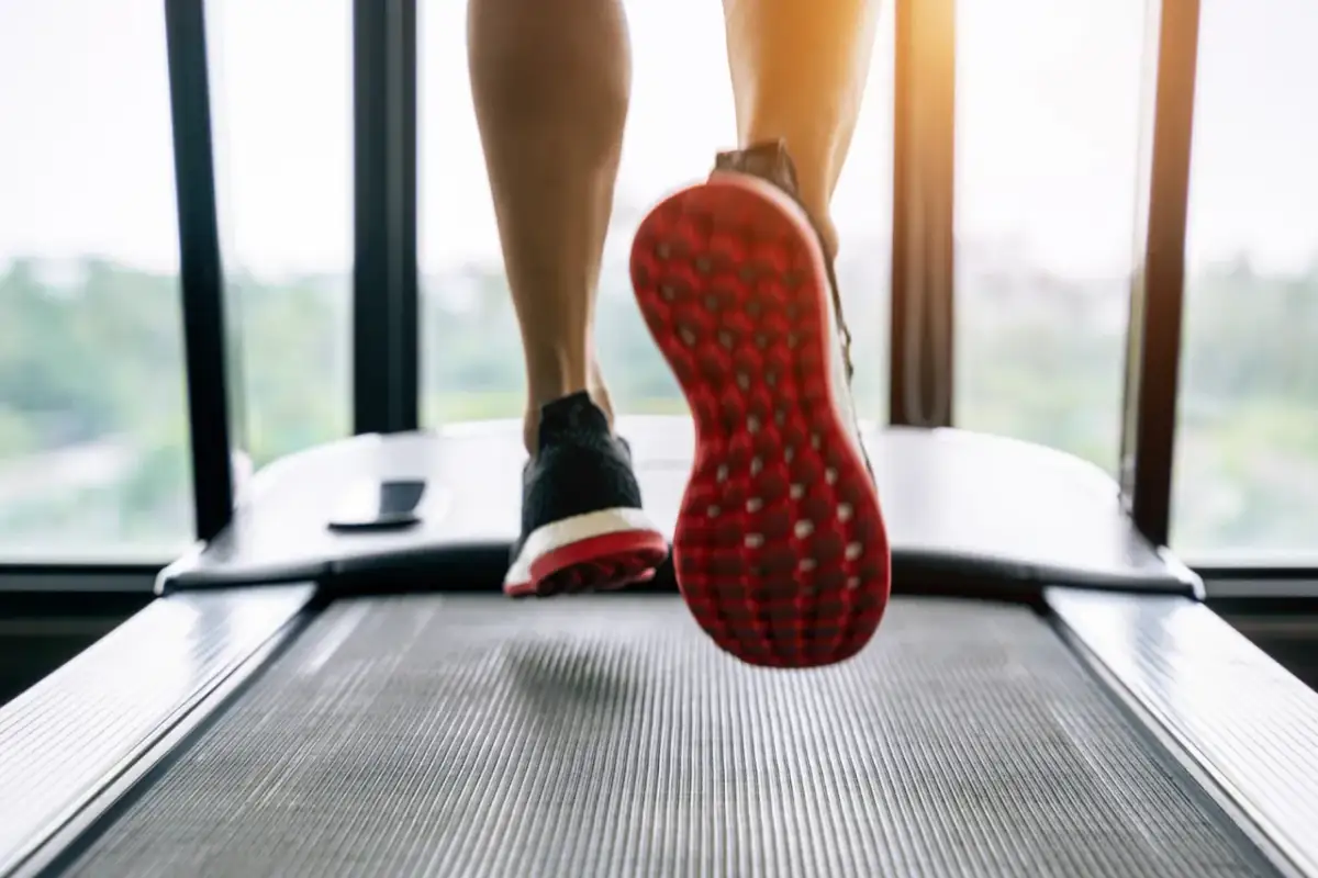 Nogi w butach sportowych biegnące po bieżni, widok z dołu.