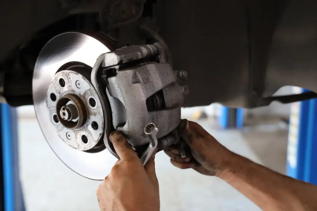 Mechanik dokręca śrubę prowadnicy z gumką góra czy dół, naprawiając hamulce samochodu.