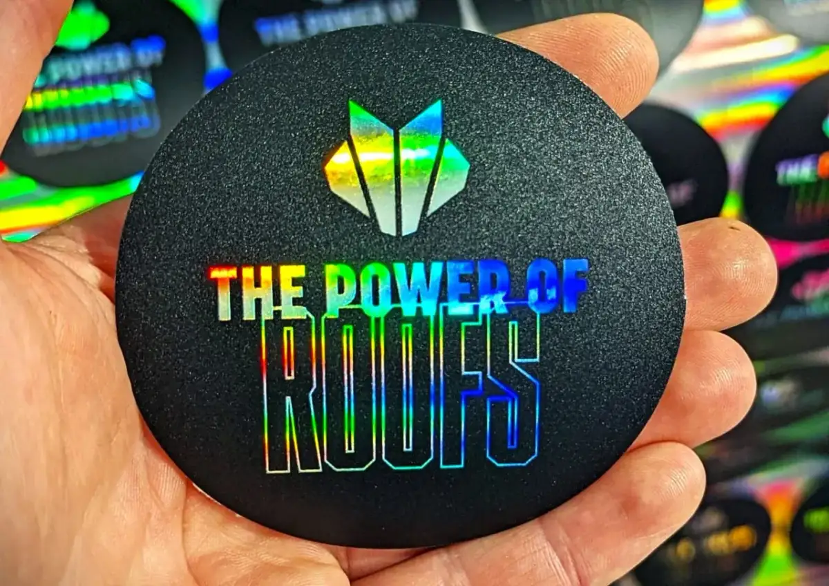 Okrągły czarny naklejka z holograficznym logo i napisem "THE POWER OF ROOFS".