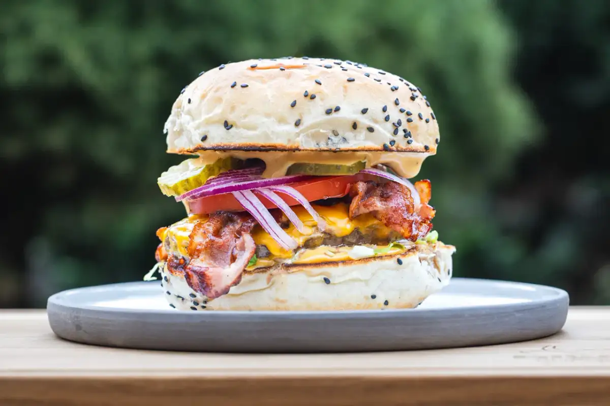 Soczysty burger z bekonem, serem i warzywami na talerzu. Idealny, by pokazać, jak jeść burgera.